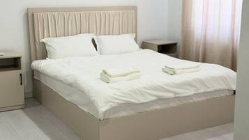 Una cama con cabecera, dos almohadas, una mesita de noche y una toalla doblada sobre la cama.
