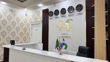 A hotel reception desk with clocks displaying different time zones, a sign indicating the hotel and apartment services, and a flag display.