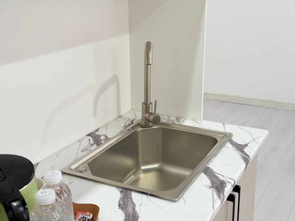 Cozinha com pia de aço inoxidável, bancada de mármore e eletrodoméstico preto à esquerda.