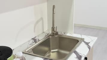 Cozinha com pia de aço inoxidável, bancada de mármore e eletrodoméstico preto à esquerda.