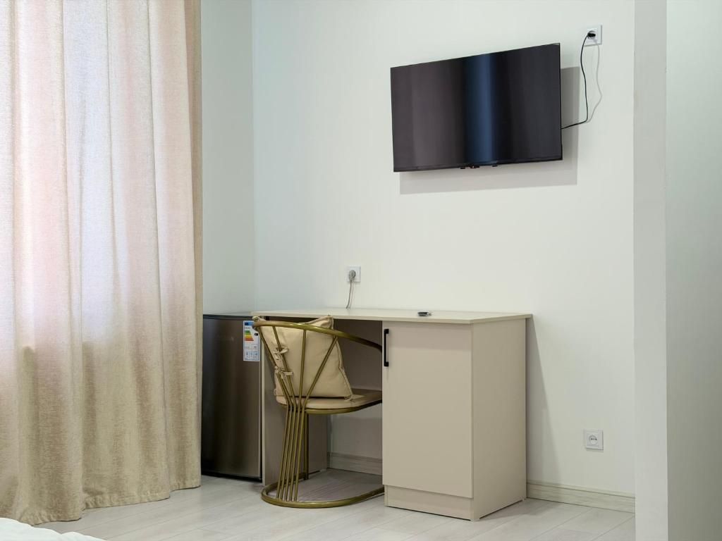 A compact room with a desk, chair, and a flat-screen TV mounted on the wall.