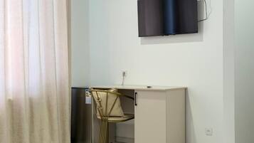 A compact room with a desk, chair, and a flat-screen TV mounted on the wall.