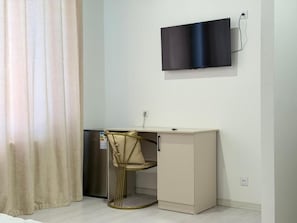 A compact room with a desk, chair, and a flat-screen TV mounted on the wall.