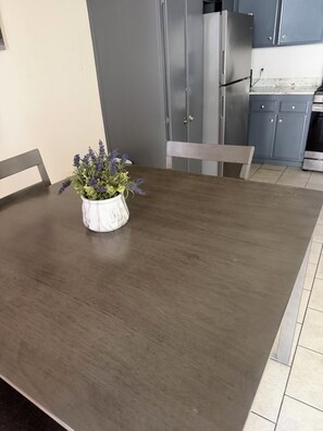 Ein Esstisch mit Stühlen, ein Blumentopf und im Hintergrund eine Küche mit Schränken und Geräten.