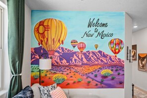 A room with a mural depicting a desert landscape and hot air balloons, a lamp, and a bed with pillows.