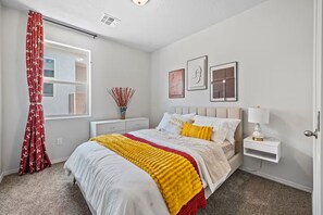 A bedroom with a bed, bedside table, lamp, and wall art.