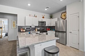 A modern kitchen with white cabinets, a granite countertop, stainless steel appliances, and a black trash bin.