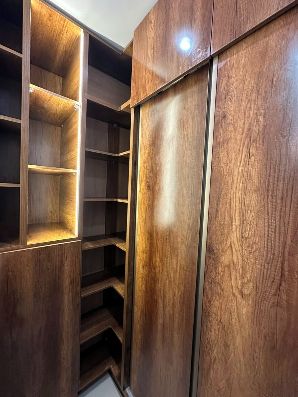 Un armario de madera con varios estantes y puerta corredera.