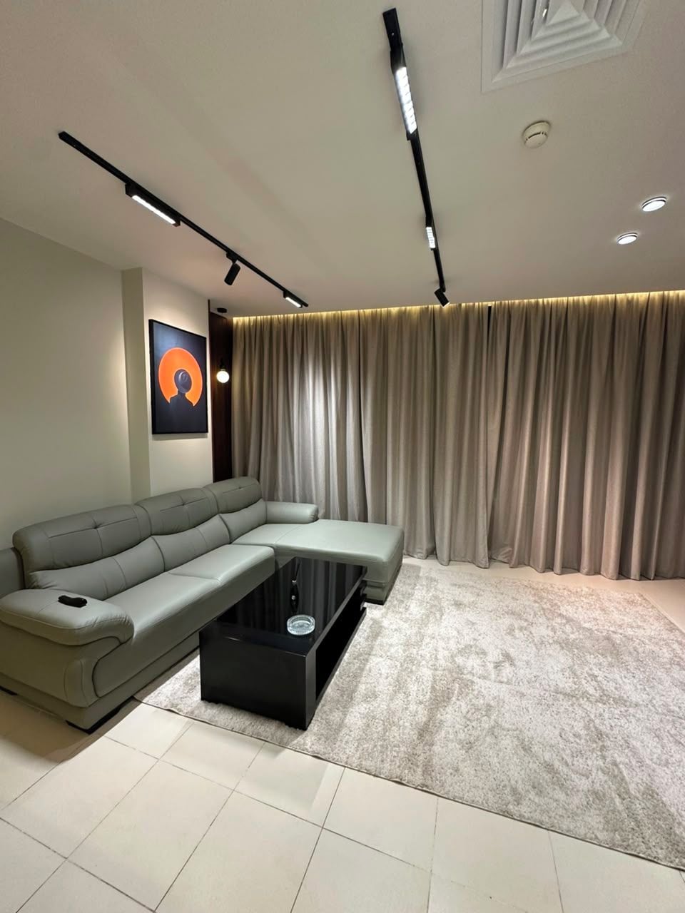 Un salon moderne avec un canapé d’angle, une table basse et une grande fenêtre agrémentée de rideaux.