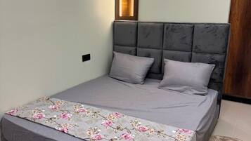 Un lit doté d’une tête de lit rembourrée de couleur grise, d’une couvre-lit à motifs floraux et de deux oreillers.