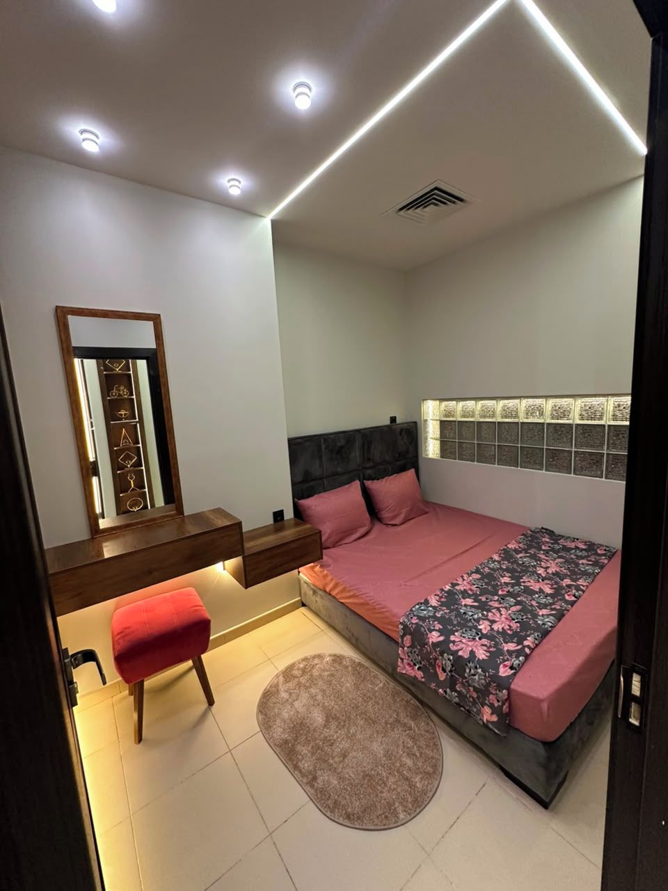A bedroom with a bed, bedside tables, a mirror, a red chair, and a rug.