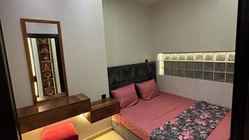 A bedroom with a bed, bedside tables, a mirror, a red chair, and a rug.