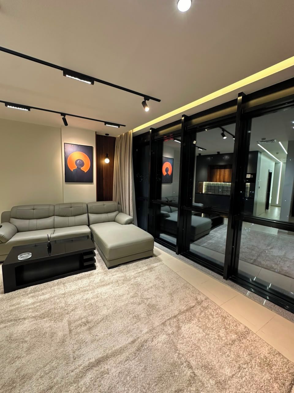 Un salon moderne avec un canapé d’angle, une table basse et une grande fenêtre agrémentée de rideaux.