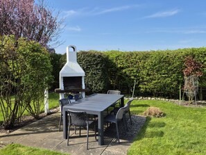 Eine Terrassenanlage im Freien mit Grill, Tisch und Stühlen.