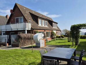 Ein zweistöckiges Haus mit einem Balkon, einem großen Fenster und einem Garten mit Tisch und Stühlen.