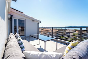 A balcony with a glass table and cushioned seating, overlooking a cityscape and water. - A2 - luxury apartment near beach with big terrace and the sea view (Kaštel Gomilica)
