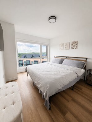 Ein Schlafzimmer mit einem großen Bett, einem Fenster mit Blick auf Gebäude und einer Deckenleuchte.