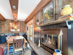 A rustic interior with a wooden dining table, benches, a fireplace, and a wall-mounted shelf with books. - New Listing - Plaza 339 — Updated 3BR Base Area Condo (Crested Butte)