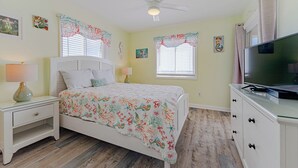 A bedroom with a bed, nightstand, dresser, TV, and two windows with curtains. - JL S-2C Sands Condos - Oceanfront - Community Pool (Kill Devil Hills)