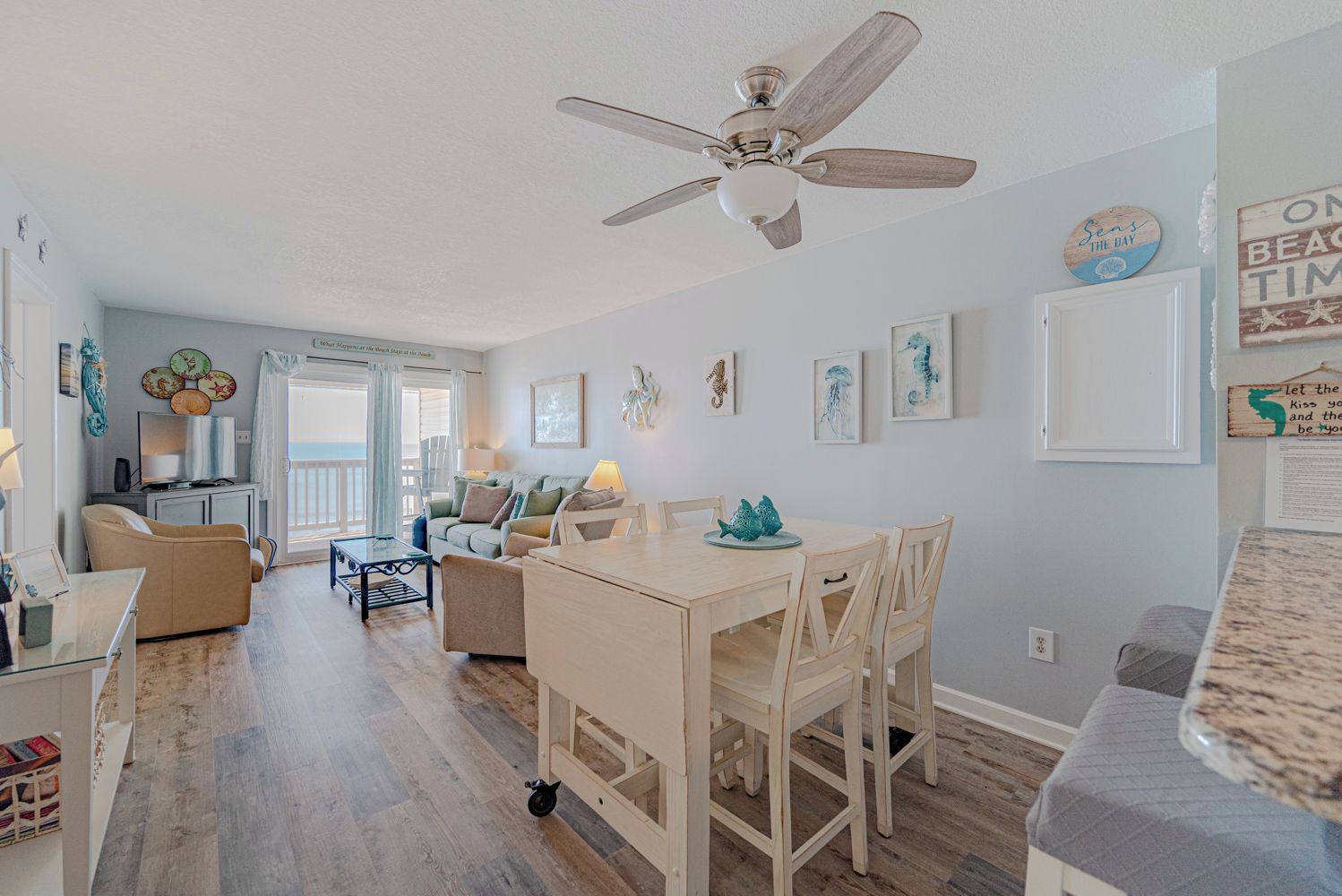 A spacious living area with a ceiling fan, a dining table with chairs, and a kitchen area in the background.