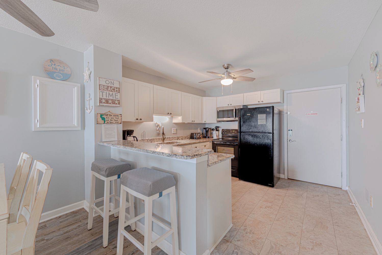 A kitchen with white cabinets, a black refrigerator, a granite countertop, and a ceiling fan.