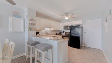 A kitchen with white cabinets, a black refrigerator, a granite countertop, and a ceiling fan.