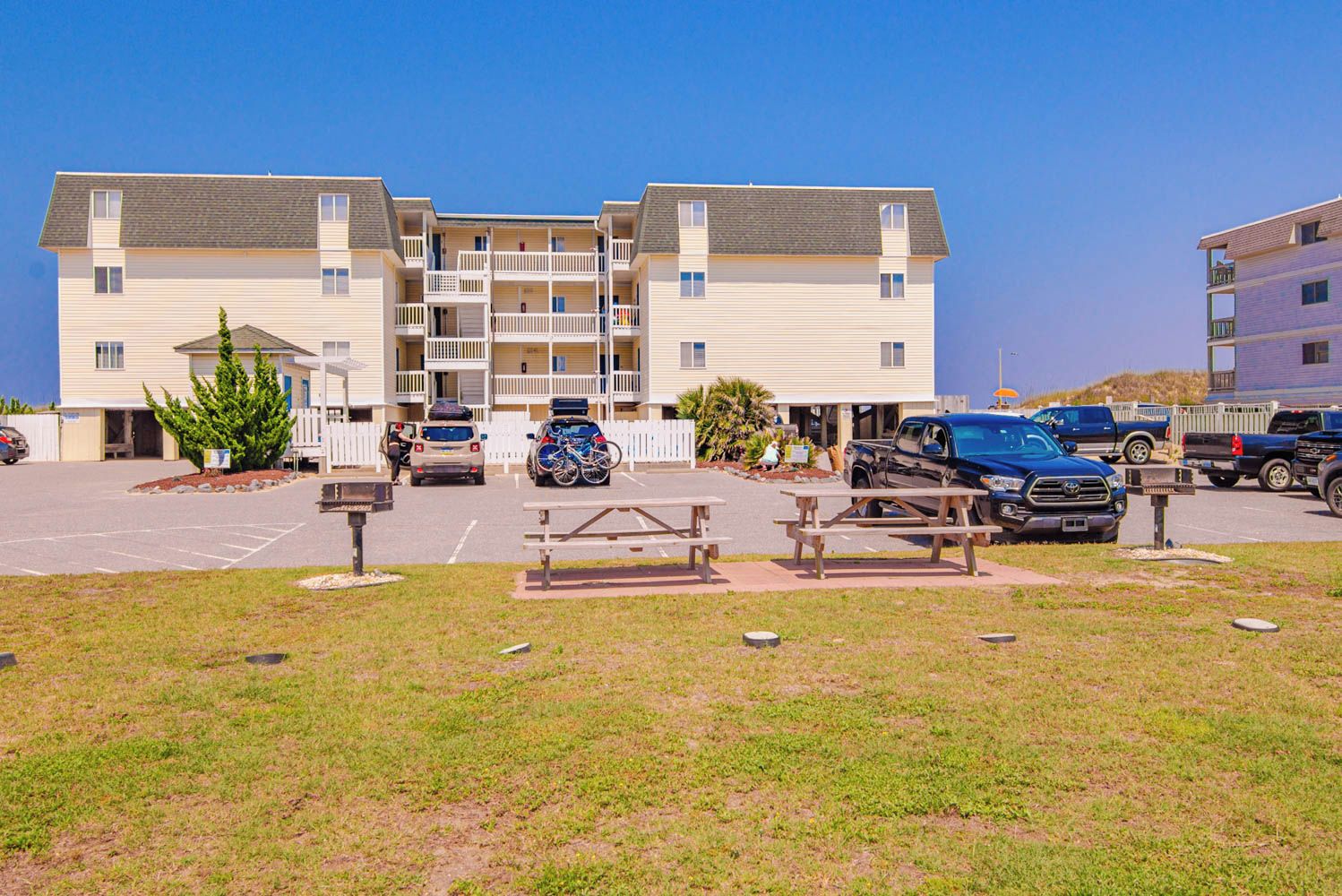 A multi-story residential building with balconies, a parking lot, and picnic tables.