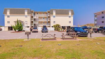 A multi-story residential building with balconies, a parking lot, and picnic tables.