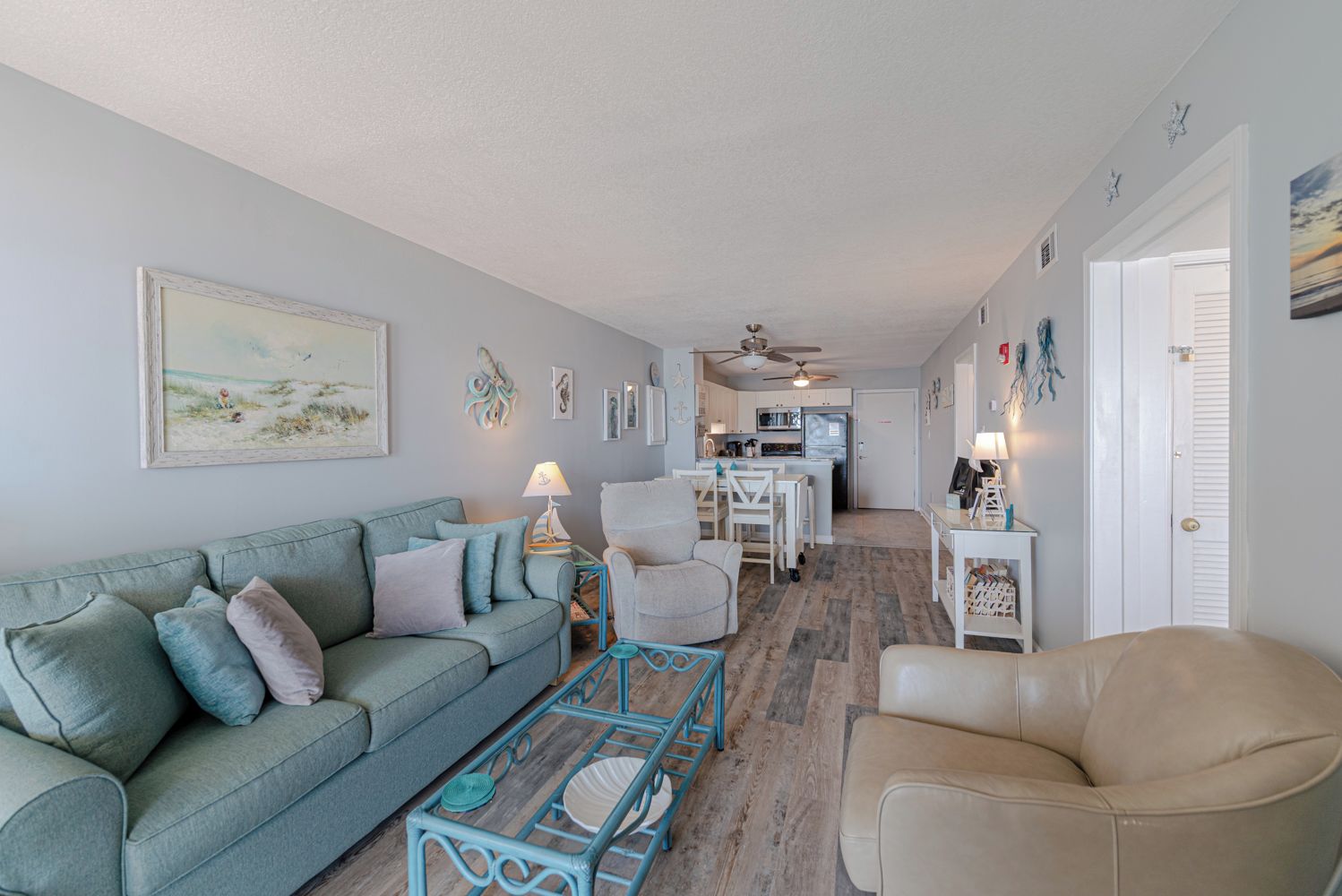 A living room with a sofa, armchair, and coffee table, leading to a kitchen area with a dining table and chairs.