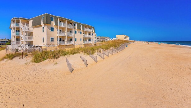 A beachfront hotel with multiple balconies, a sandy beach, and a clear blue sky. - JL S-2C Sands Condos - Oceanfront - Community Pool (Kill Devil Hills)