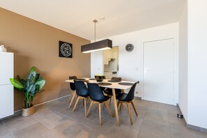 A modern dining area with a white table, black chairs, and a hanging light fixture. - Apartment in Blankenberge With Sea Views (Blankenberge)