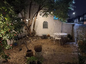 Ein Garten mit Tisch und Stühlen, einem kleinen Fenster und Lichterketten.
