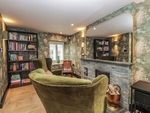 Ein gemütliches Wohnzimmer mit Kamin, Bücherregalen, einem grünen Sessel und einem großen Spiegel.