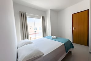 Ein Hotelzimmer mit einem Bett, einem Fenster mit Vorhängen, einer Tür und Blick nach außen.