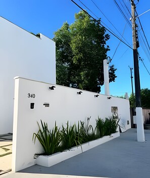 Un bâtiment blanc, portant le numéro 940 sur sa façade, entouré de verdure et surplombé d’un ciel bleu clair.