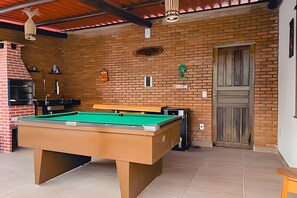 Une table de billard dans une pièce avec un mur en briques, une porte en bois et une cheminée en briques.