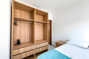 A bedroom with a large wooden wardrobe, a bed with white bedding, and a bedside table with a lamp. - Apartamento 2 com 2 suítes 450m da praia (Santa Cruz Cabrália)