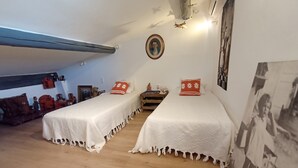 Et værelse med to senge, trægulv, loftlampe og et billede i ramme på væggen.