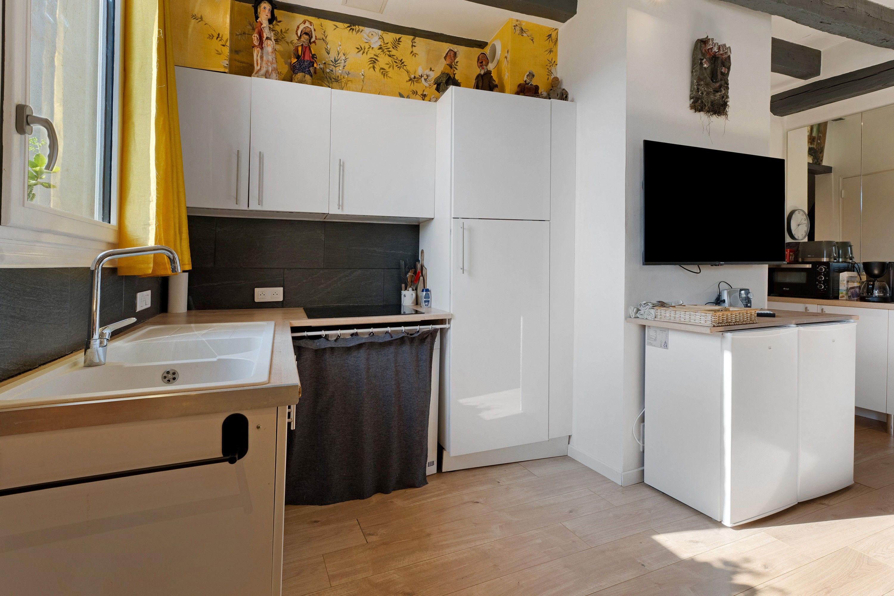 Eine moderne Küche mit weißen Schränken, einem Einbauofen, einer Spüle und einem an der Wand befestigten Flachbildfernseher.