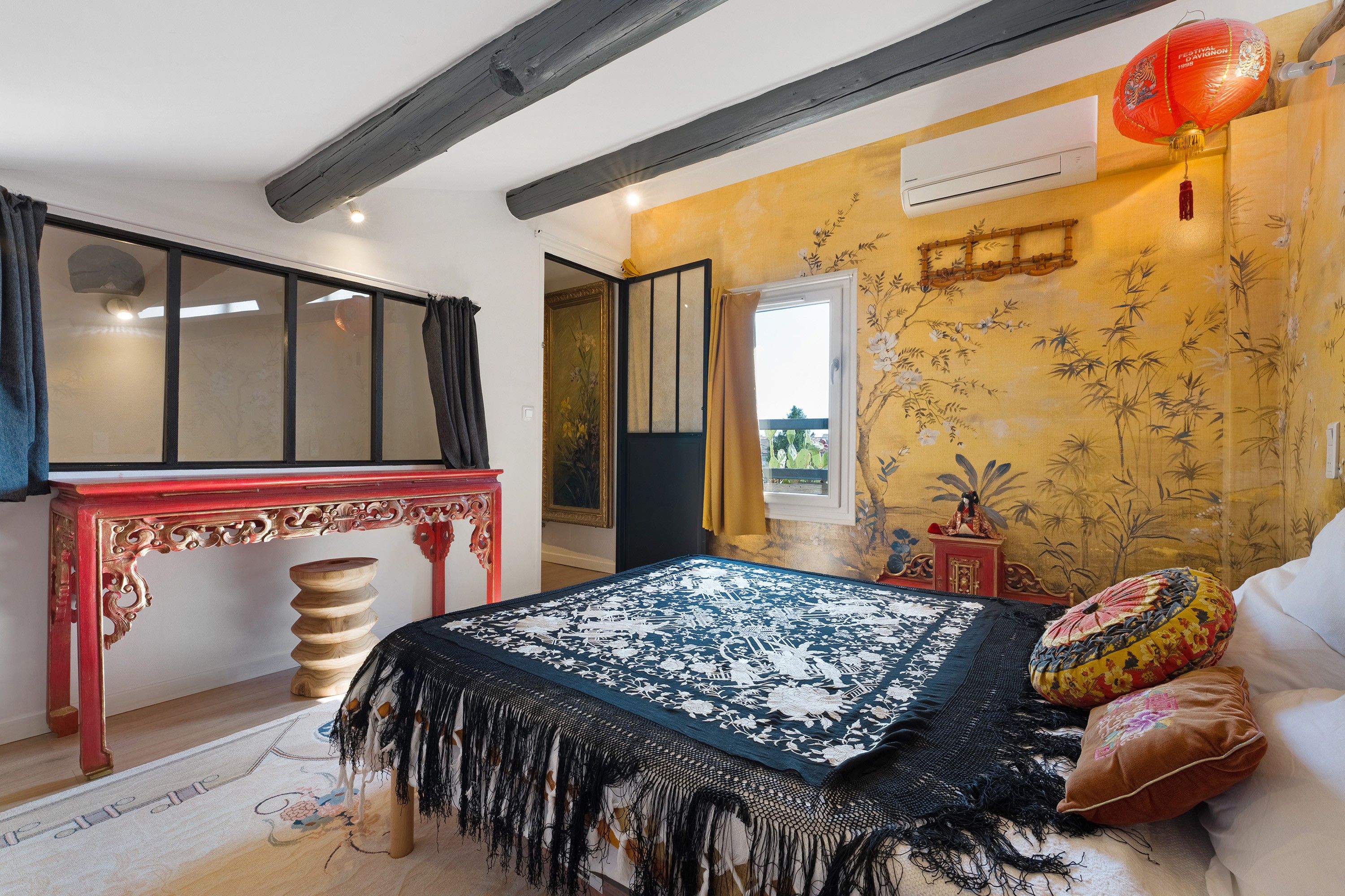 Ein Schlafzimmer mit einem Bett, einem roten Tisch, einem Fenster und einer blumengedeckten Wand.