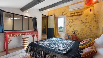 Ein Schlafzimmer mit einem Bett, einem roten Tisch, einem Fenster und einer blumengedeckten Wand.