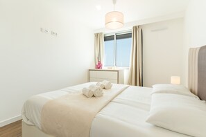 Ein Hotelzimmer mit Bett, Nachttisch, einem Fenster mit Vorhängen und einer Pendelleuchte.