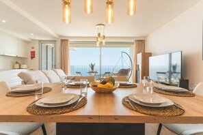 Ein moderner Essbereich mit einem Holztisch, gedeckt für vier Personen, umgeben von weißen Sofas, und einem Balkon mit Blick.