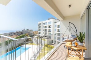 Ein Balkon mit Blick auf einen Swimmingpool, einem Hängesessel und einem Tisch mit einem Blumentopf.