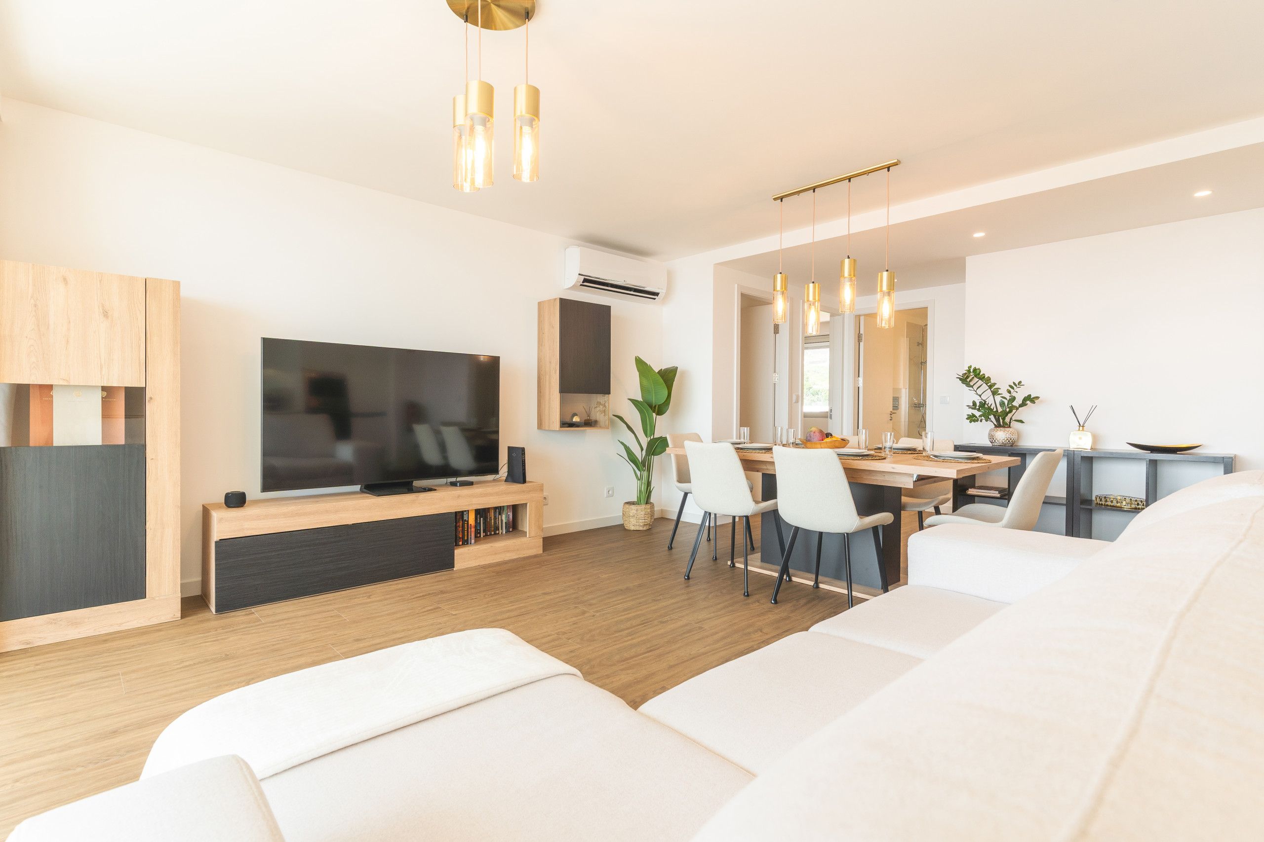 Un salon moderne doté d’un téléviseur à écran plat, de meubles en bois et d’un coin repas avec des chaises et une table.