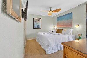 Ein Hotelzimmer mit Bett, Deckenventilator, Gemälde und Wandfernseher.