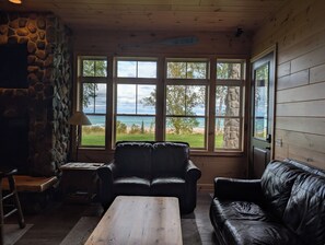 A room with a stone wall, a wooden ceiling, a view of the beach, and two leather sofas. - The Ridge! Amazing view of Lake Superior, close to downtown & room for all (Grand Marais)