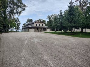 A two-story building with a garage, surrounded by a gravel driveway and trees. - The Ridge! Amazing view of Lake Superior, close to downtown & room for all (Grand Marais)