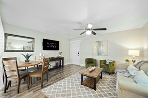 A living room with a dining area, a ceiling fan, a flat-screen TV, and a painting on the wall. - Elegant 2BR Apartment right by Cowboys Stadium! (Arlington)
