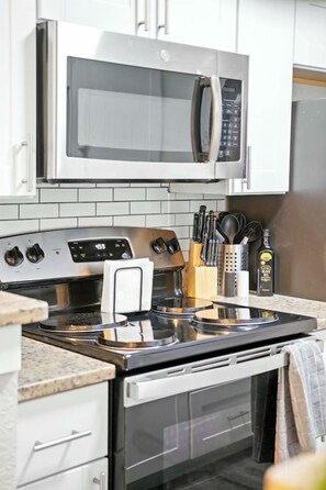 A kitchen with a stainless steel stove, microwave, and oven. There are cabinets above the stove and a countertop with a knife block and a bottle. - Elegant 2BR Apartment right by Cowboys Stadium! (Arlington)